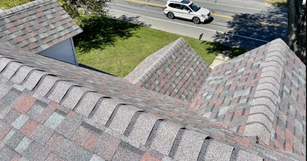 Chris Battaini Roofing - A close-up view of a shingled house roof with a street and a white SUV visible in the background.
