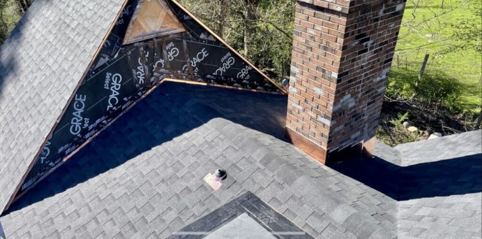 Chris Battaini Roofing - A house roof with gray shingles, a brick chimney, and an unfinished dormer section covered with black waterproofing material.